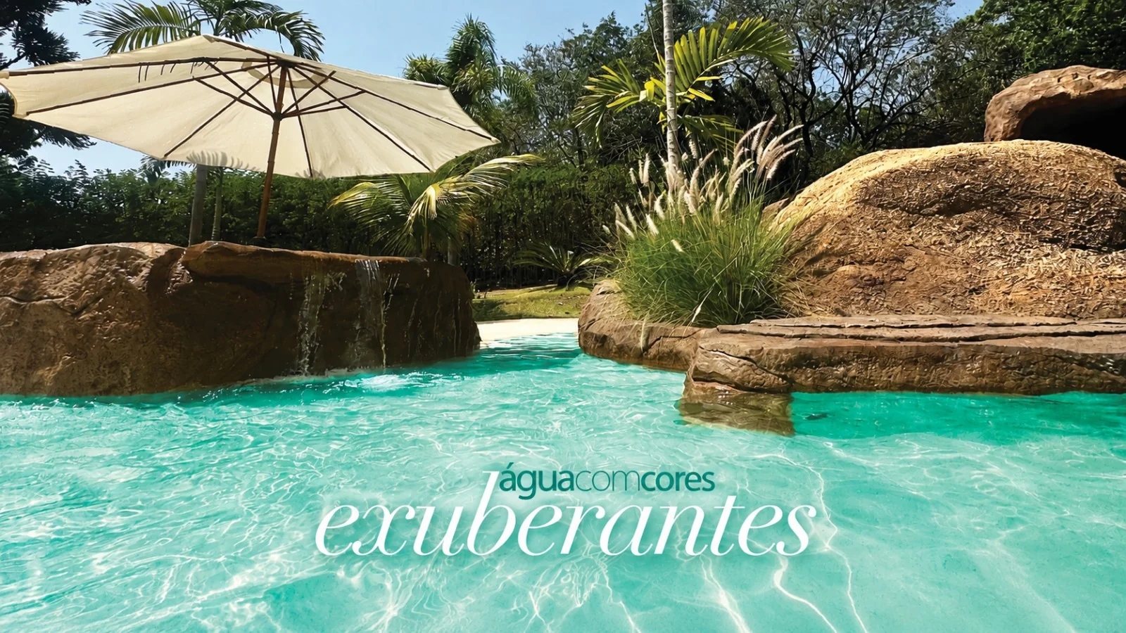 Piscina com água em cores exuberantes, com ombrelone e rochas