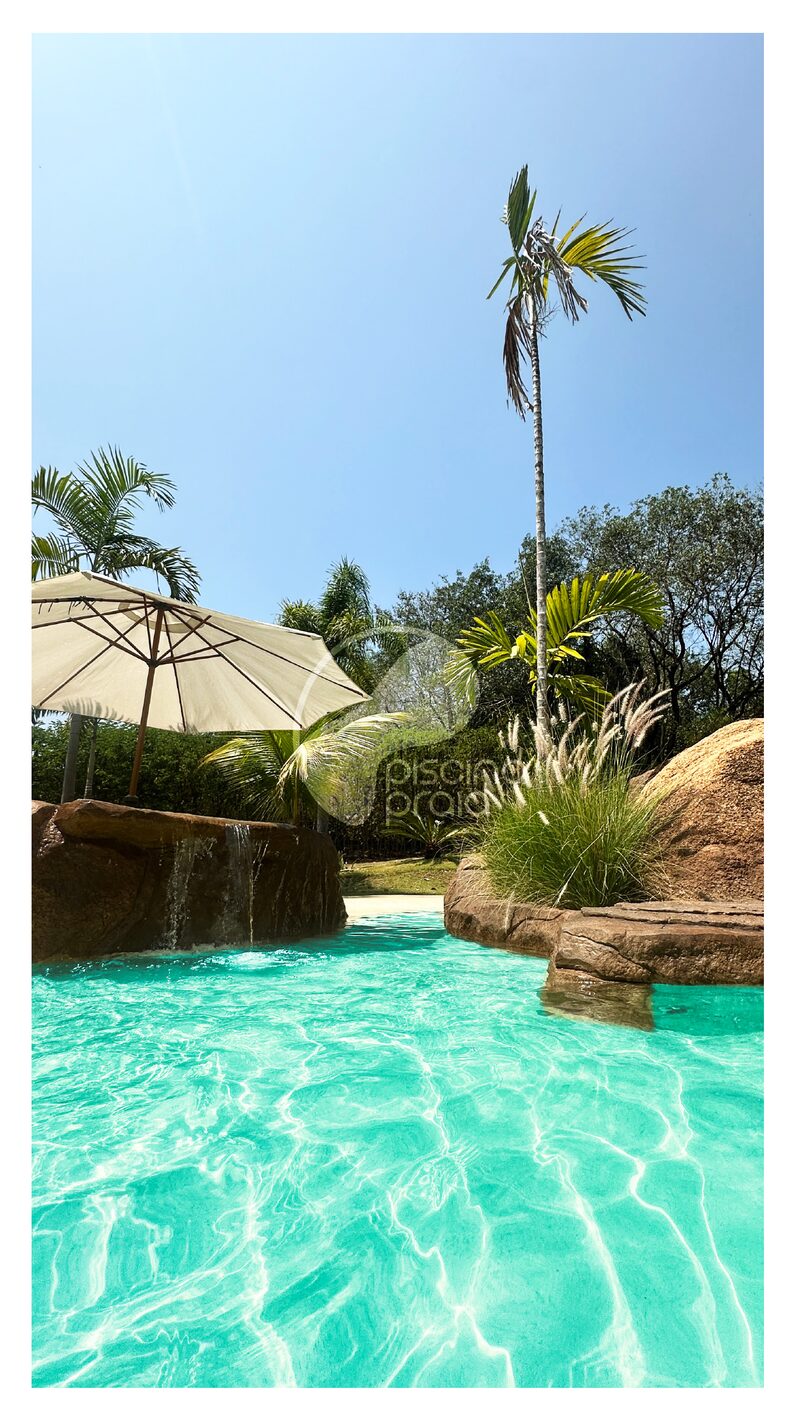 Piscina de água turquesa com guarda-sol de palha, rochas e coqueiros
