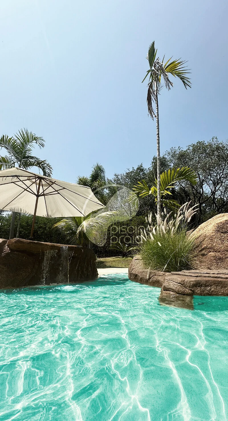 Piscina de água turquesa com guarda-sol de palha, rochas e coqueiros