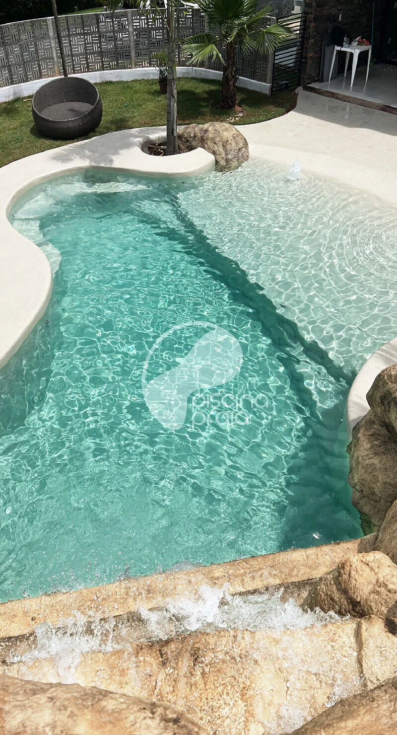 Piscina de borda orgânica com rochas, jardim tropical e balanço suspenso
