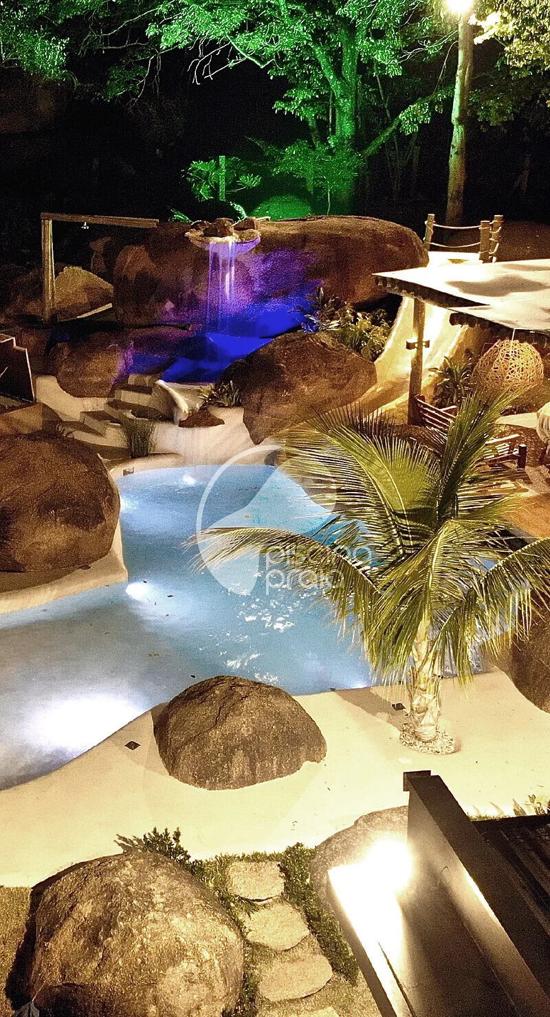 Piscina noturna entre rochas, com iluminação azul e deck de madeira
