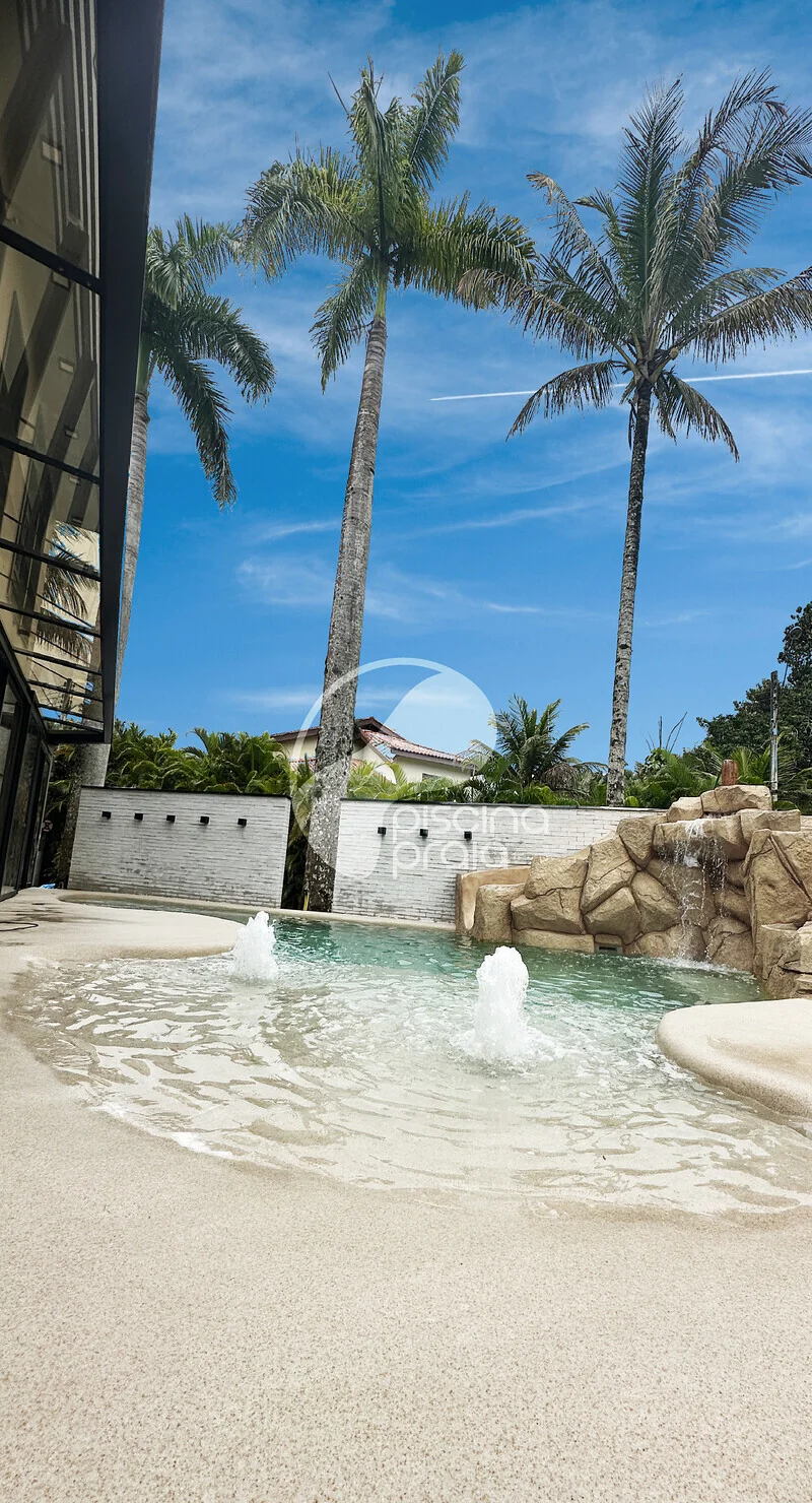 Piscina com jatos de água, prainha de areia e coqueiros altos