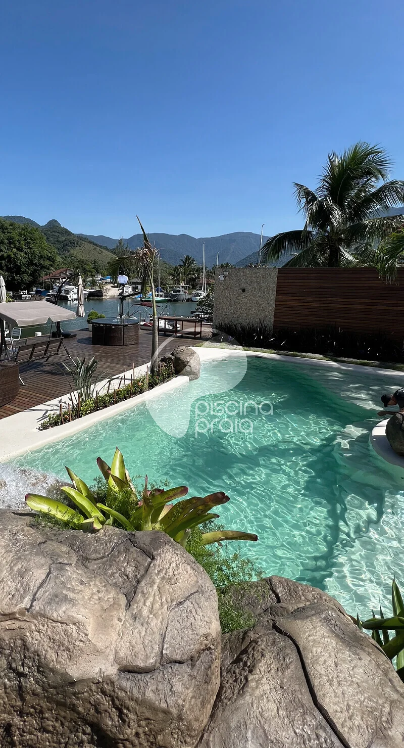 Piscina com rochas e deck de madeira, com montanhas ao fundo