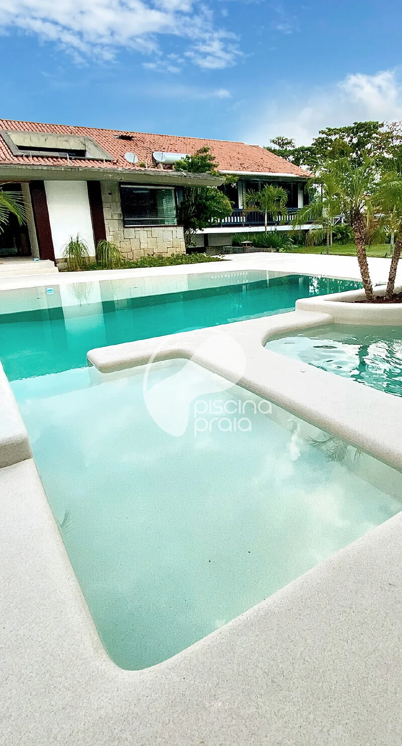 Piscina residencial com prainha de acesso e a casa ao fundo