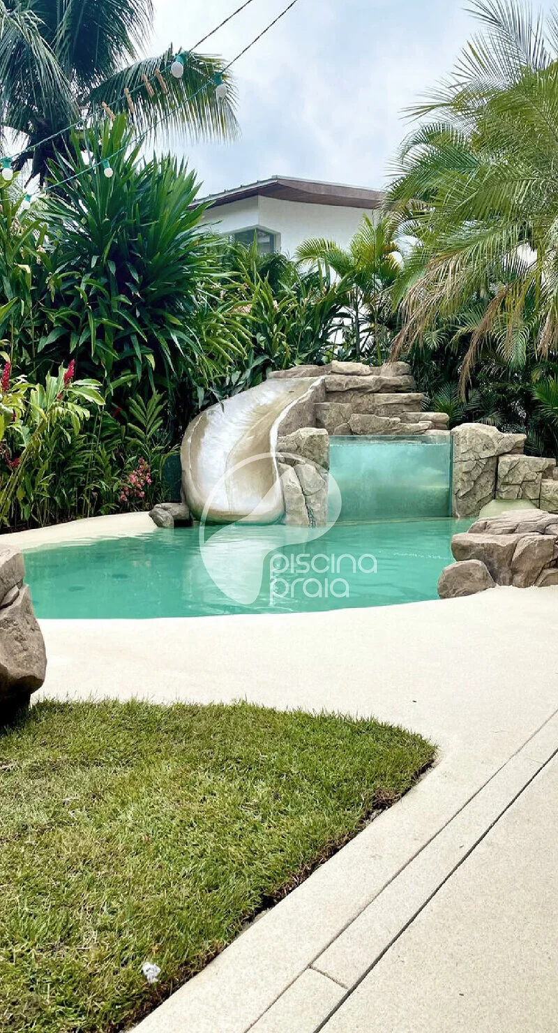 Piscina com escorregador de rocha, gramado e jardim tropical