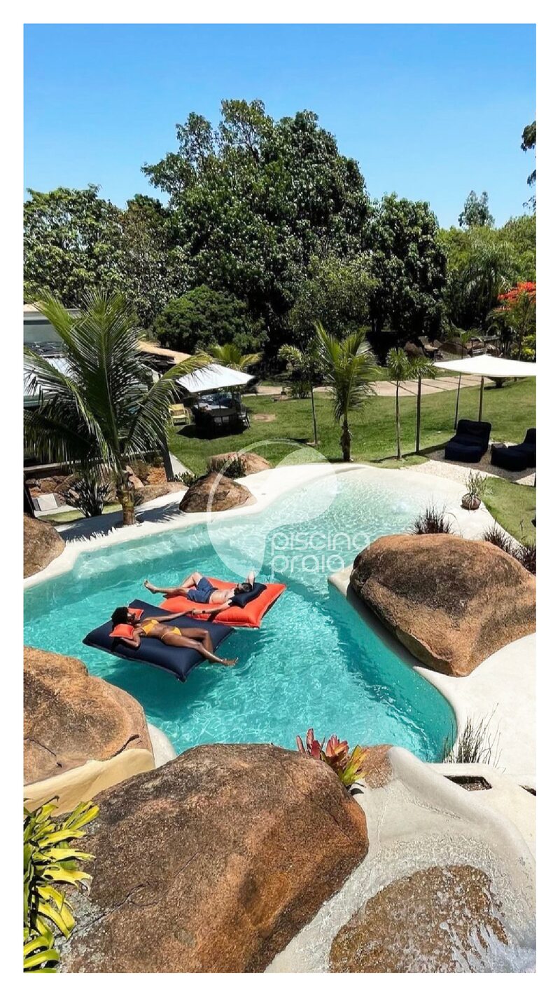 Piscina com rochas e boias, com pessoas tomando sol na prainha