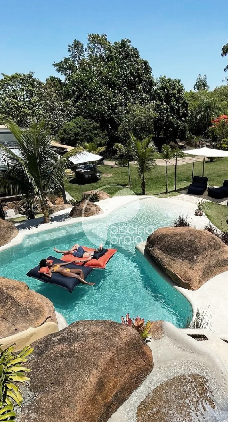 Piscina com rochas e boias, com pessoas tomando sol na prainha