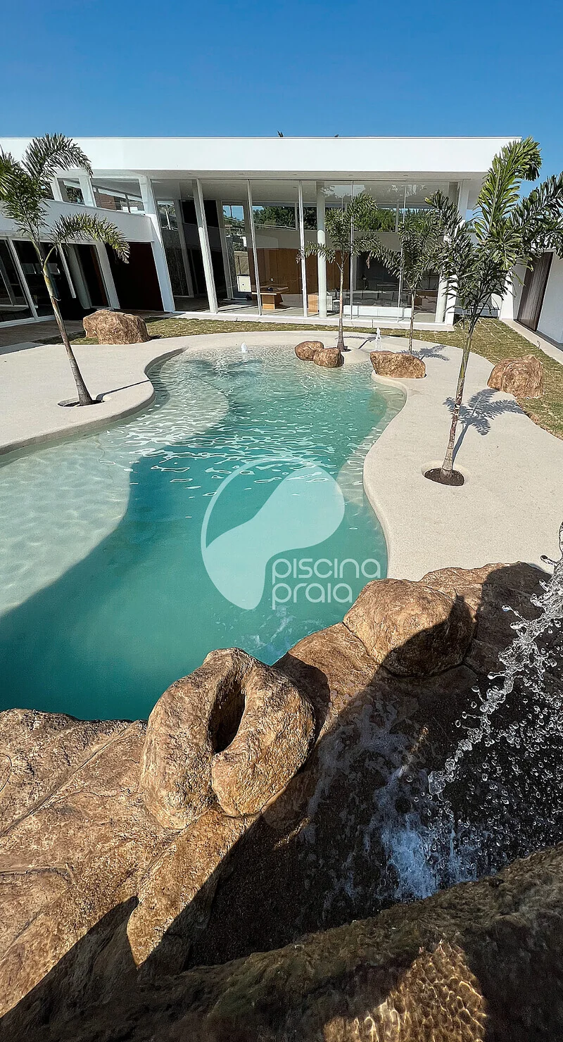 Piscina com cascata de rochas em frente à casa de vidro