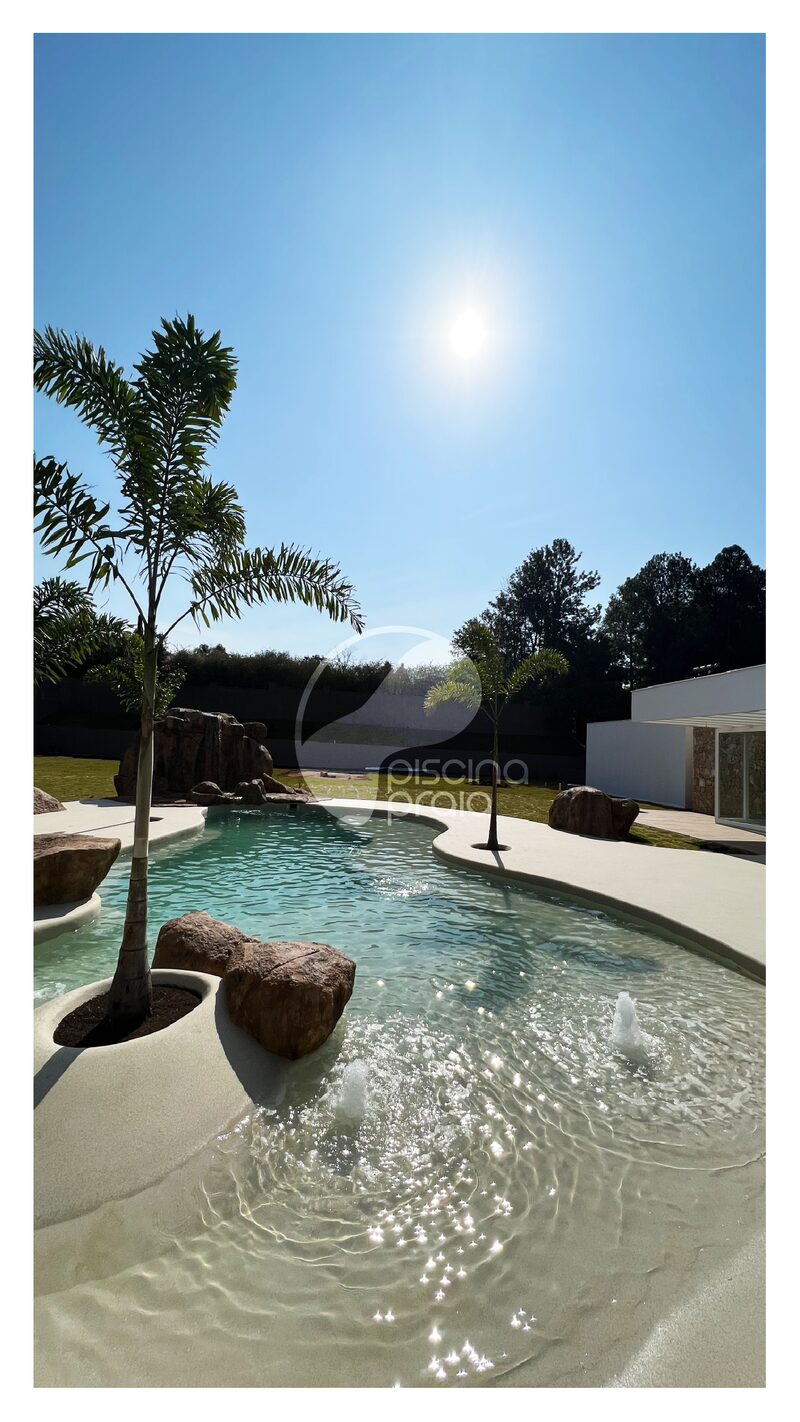 Piscina com ilha de coqueiro e pedra, sob o sol forte