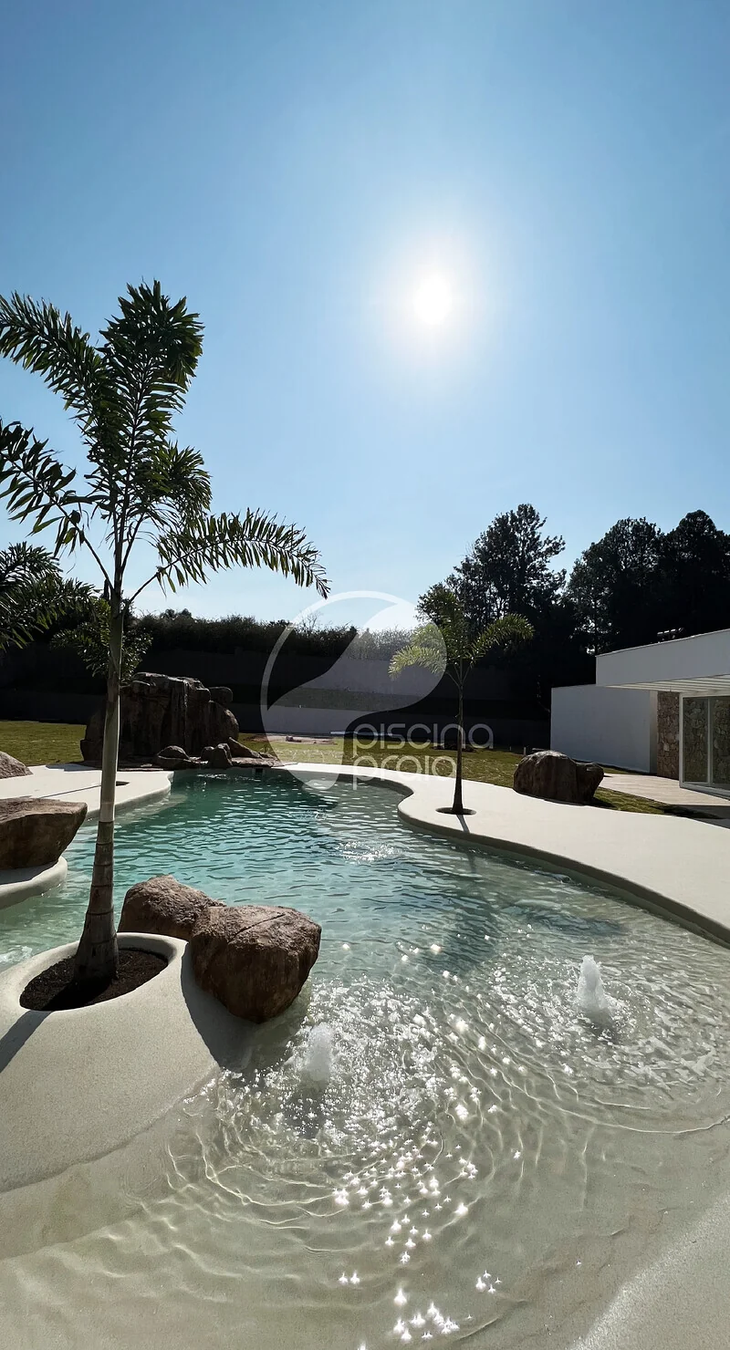 Piscina com ilha de coqueiro e pedra, sob o sol forte